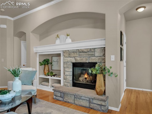 living area with a stone fireplace, hardwood / wood-style flooring, and ornamental molding