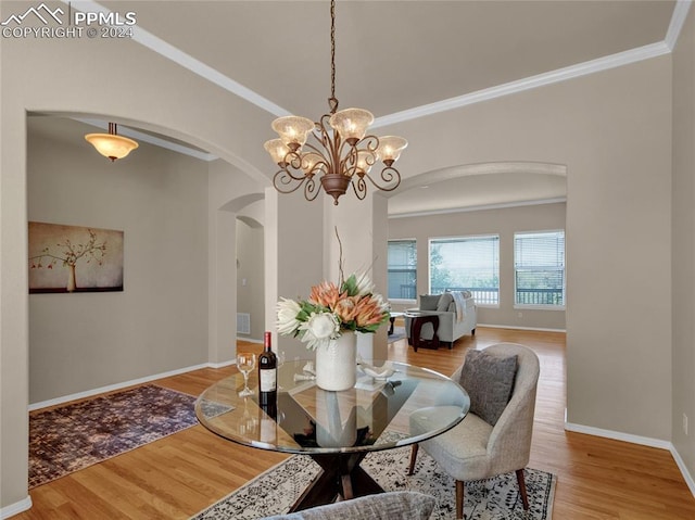 dining area with wood-type flooring, an inviting chandelier, and ornamental molding