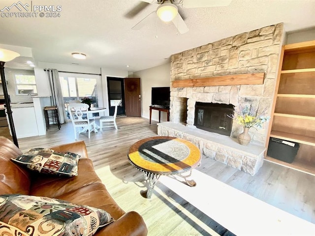 living room featuring light hardwood / wood-style floors, ceiling fan, vaulted ceiling, a fireplace, and a textured ceiling