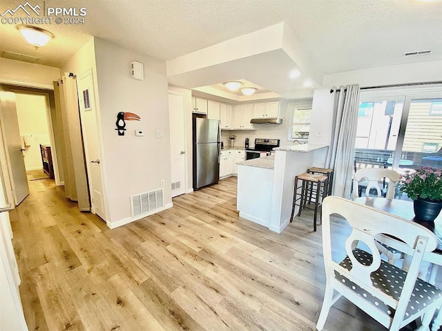 kitchen with stainless steel appliances, kitchen peninsula, a healthy amount of sunlight, and white cabinetry