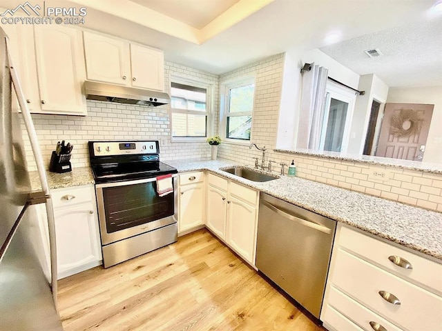 kitchen featuring light wood-type flooring, sink, decorative backsplash, light stone countertops, and appliances with stainless steel finishes