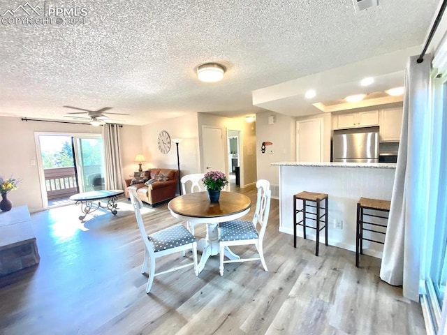 dining space with ceiling fan, a textured ceiling, and light wood-type flooring