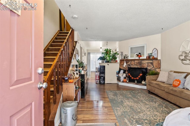 living room with a textured ceiling, hardwood / wood-style floors, and a stone fireplace