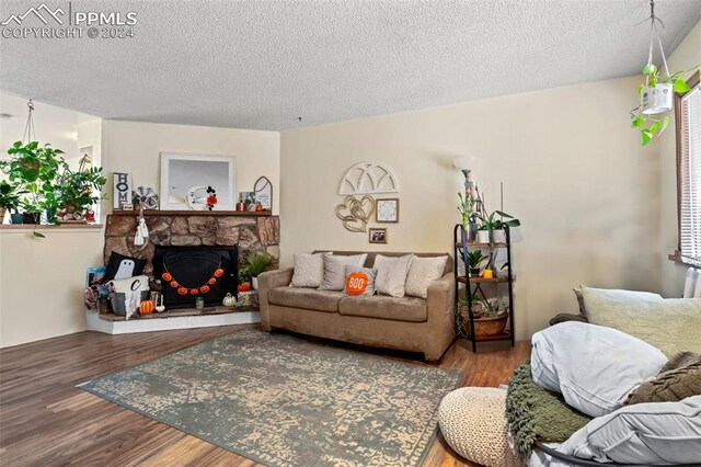 living room with a textured ceiling, a stone fireplace, and hardwood / wood-style flooring