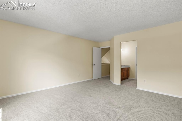 unfurnished bedroom featuring light carpet, a textured ceiling, and connected bathroom