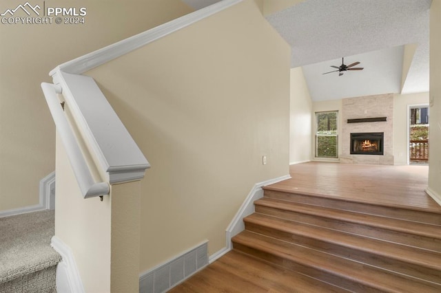 staircase featuring ceiling fan, lofted ceiling, a textured ceiling, hardwood / wood-style flooring, and a fireplace