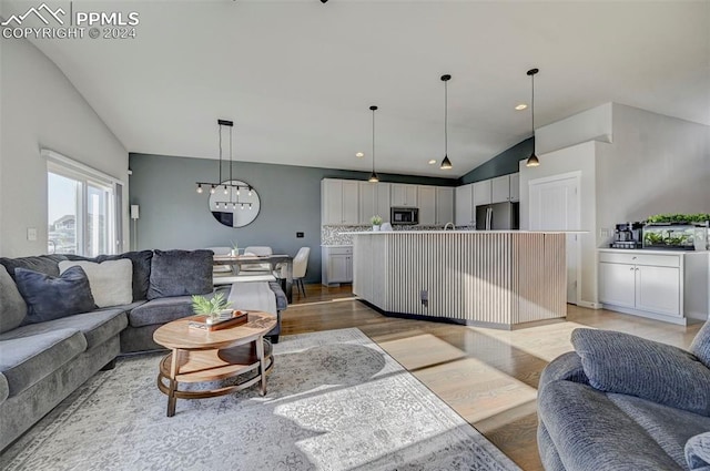 living room featuring a notable chandelier, light hardwood / wood-style flooring, and vaulted ceiling