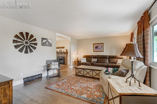 living room with a brick fireplace and hardwood / wood-style floors