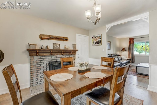 dining area featuring a brick fireplace, a notable chandelier, and light wood-type flooring