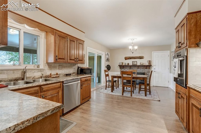 kitchen featuring hanging light fixtures, sink, backsplash, stainless steel appliances, and light wood-type flooring