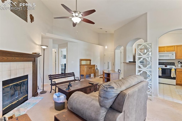 carpeted living room with a tiled fireplace, ceiling fan, and high vaulted ceiling