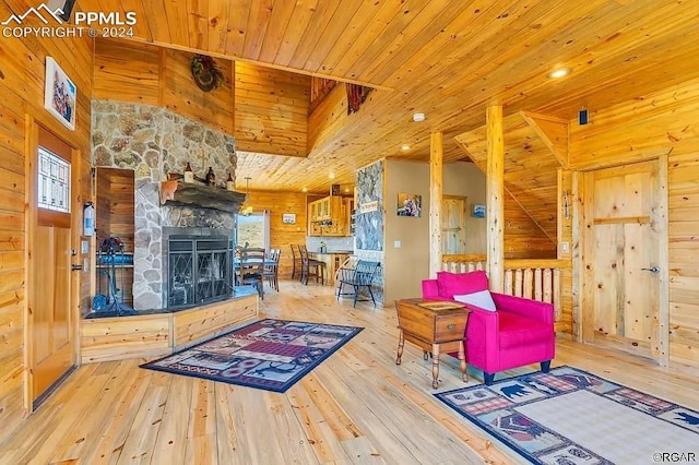 living room with light wood-type flooring, wooden walls, a stone fireplace, and wood ceiling