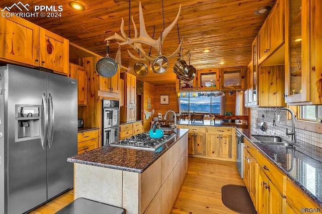 kitchen with light hardwood / wood-style floors, dark stone counters, a center island with sink, sink, and stainless steel appliances