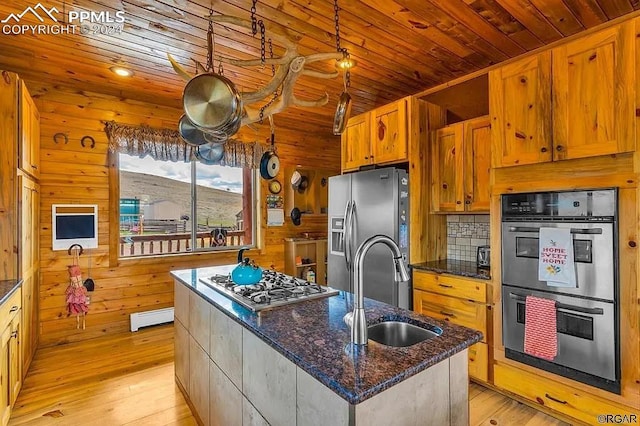 kitchen featuring a kitchen island with sink, light wood-type flooring, sink, wooden walls, and appliances with stainless steel finishes