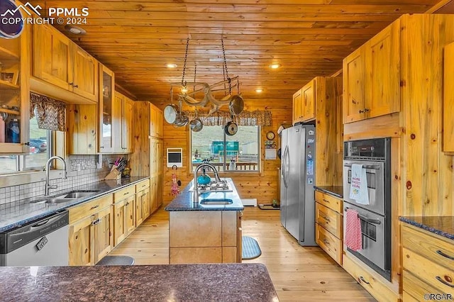 kitchen featuring an island with sink, wooden walls, sink, light hardwood / wood-style flooring, and appliances with stainless steel finishes