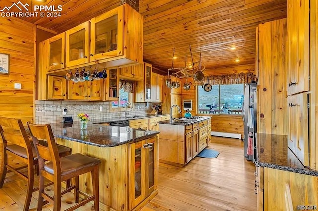 kitchen featuring wood walls, kitchen peninsula, a center island with sink, and light wood-type flooring