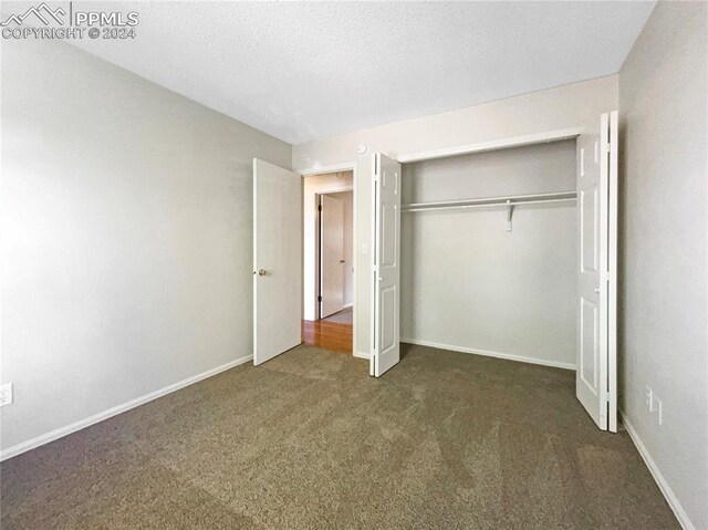 unfurnished bedroom with dark carpet, a closet, and a textured ceiling