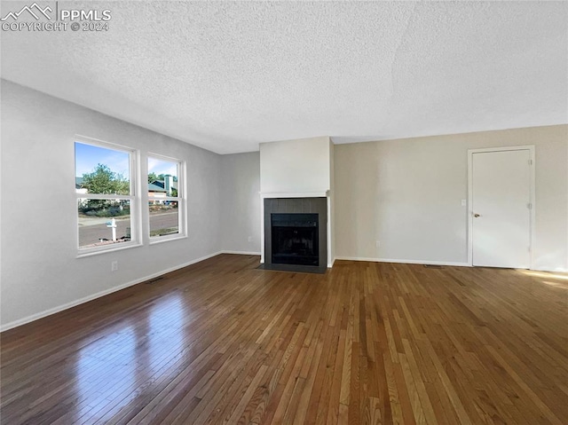 unfurnished living room featuring a textured ceiling, a tiled fireplace, and dark wood-type flooring