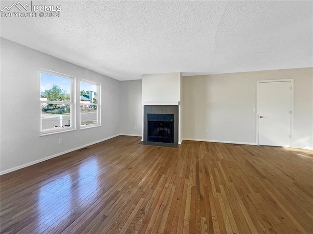 unfurnished living room with a tiled fireplace, a textured ceiling, and dark hardwood / wood-style flooring