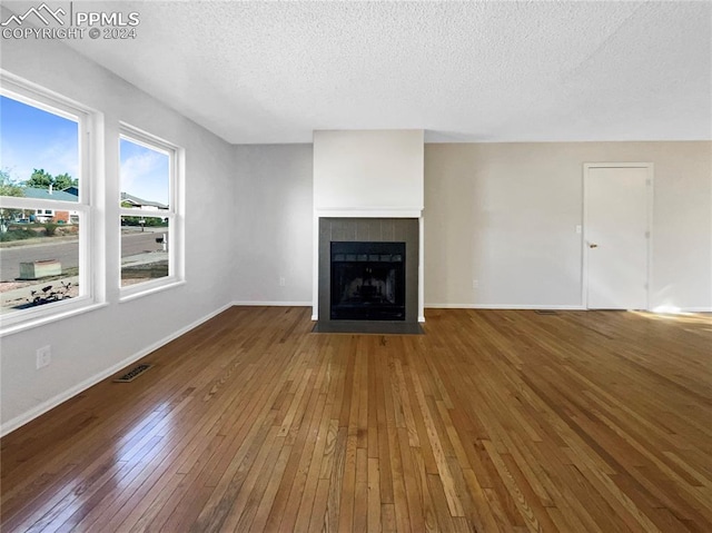 unfurnished living room with wood-type flooring, a tiled fireplace, and a textured ceiling