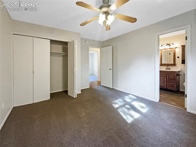 unfurnished bedroom with a closet, dark colored carpet, ceiling fan, ensuite bathroom, and sink