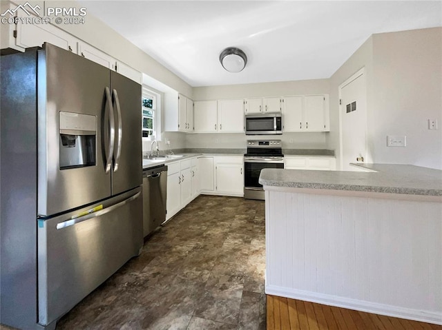 kitchen with appliances with stainless steel finishes, kitchen peninsula, white cabinetry, and sink