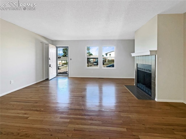 unfurnished living room featuring a tiled fireplace, a textured ceiling, and dark wood-type flooring