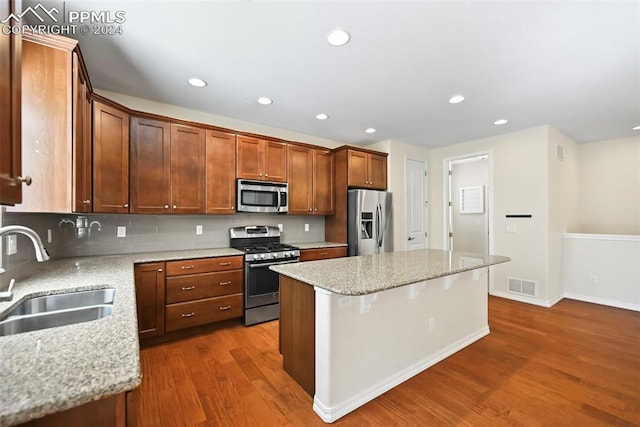 kitchen with a kitchen island, light stone countertops, stainless steel appliances, hardwood / wood-style floors, and sink