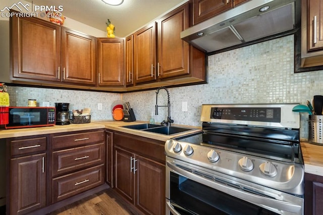 kitchen with decorative backsplash, hardwood / wood-style floors, exhaust hood, stainless steel range oven, and sink