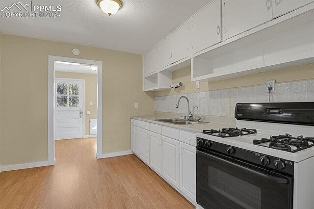 kitchen featuring white cabinets, sink, tasteful backsplash, light hardwood / wood-style flooring, and white gas range oven