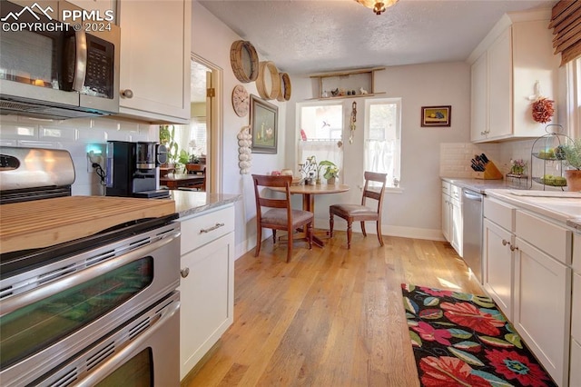 kitchen featuring appliances with stainless steel finishes, decorative backsplash, white cabinetry, a textured ceiling, and light hardwood / wood-style flooring