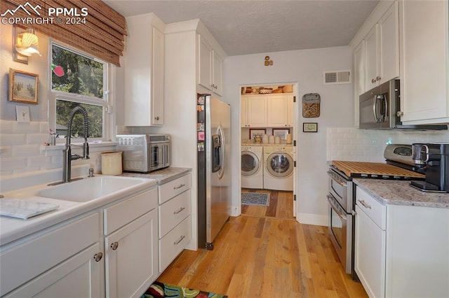 kitchen featuring appliances with stainless steel finishes, washing machine and dryer, tasteful backsplash, white cabinets, and light hardwood / wood-style flooring