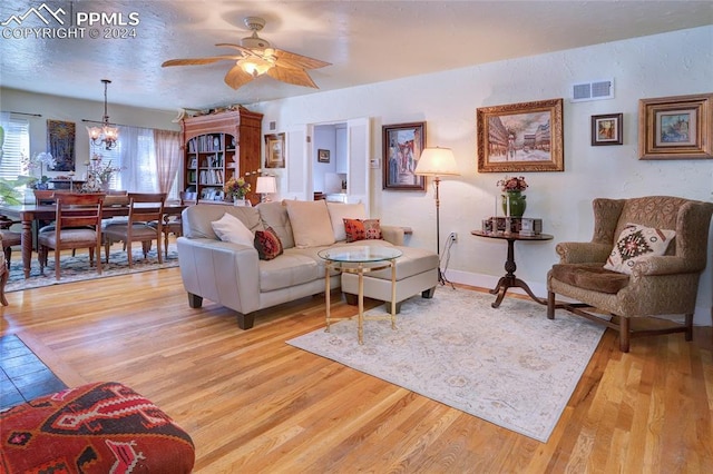 living room with ceiling fan with notable chandelier and light hardwood / wood-style floors