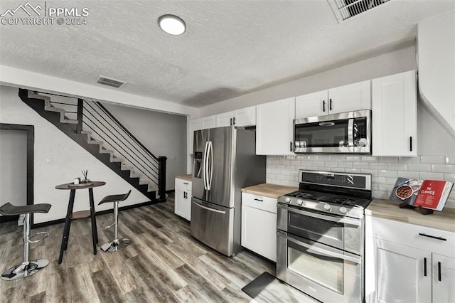 kitchen with appliances with stainless steel finishes, decorative backsplash, white cabinetry, a textured ceiling, and hardwood / wood-style flooring