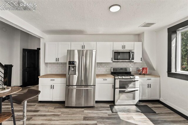 kitchen featuring stainless steel appliances, white cabinetry, and butcher block counters