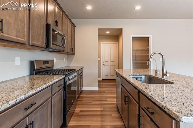 kitchen with light stone countertops, sink, stainless steel appliances, and light wood-type flooring