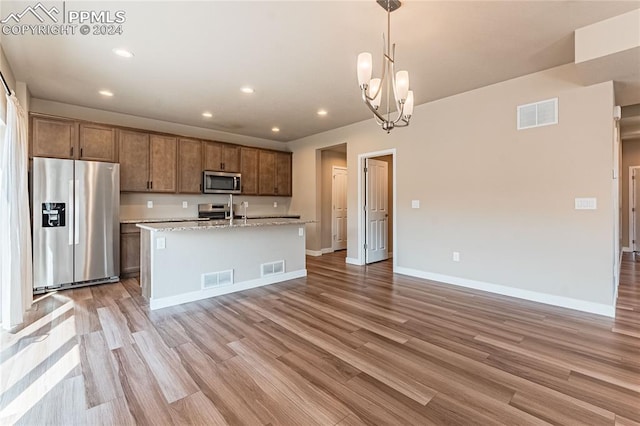 kitchen with light hardwood / wood-style floors, a center island with sink, hanging light fixtures, and appliances with stainless steel finishes