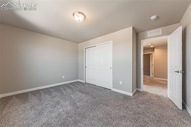 unfurnished bedroom with a textured ceiling, carpet floors, and a closet