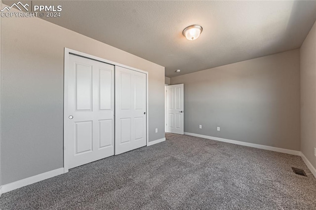 unfurnished bedroom featuring a textured ceiling, dark carpet, and a closet