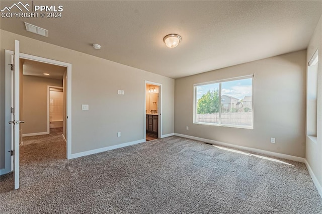 unfurnished bedroom with ensuite bath, carpet floors, and a textured ceiling