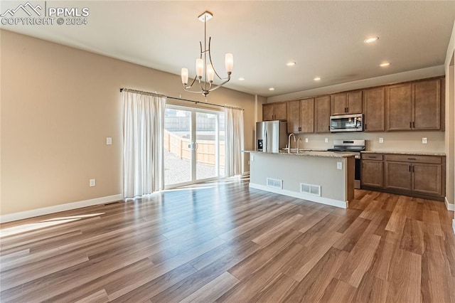 kitchen featuring pendant lighting, stainless steel appliances, a kitchen island with sink, and hardwood / wood-style floors