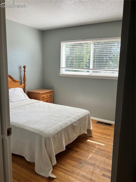 bedroom with a textured ceiling, light hardwood / wood-style flooring, and multiple windows