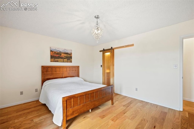 bedroom with a notable chandelier, a barn door, and light hardwood / wood-style flooring