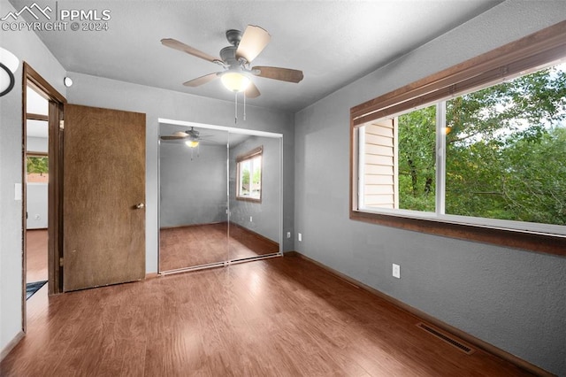 unfurnished bedroom with ceiling fan, wood-type flooring, a closet, and multiple windows