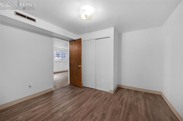 unfurnished bedroom featuring a textured ceiling, a closet, and dark hardwood / wood-style floors