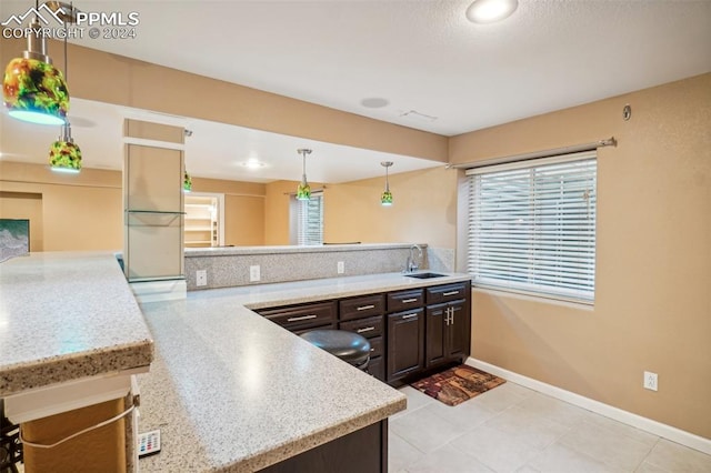 kitchen with pendant lighting, sink, kitchen peninsula, dark brown cabinets, and a kitchen bar