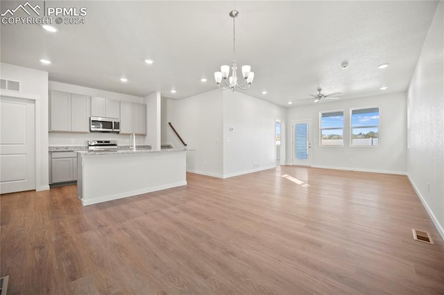 kitchen with light wood-type flooring, light stone counters, an island with sink, gray cabinetry, and stainless steel appliances