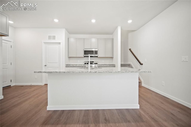 kitchen featuring wood-type flooring, a center island with sink, light stone countertops, and gray cabinets