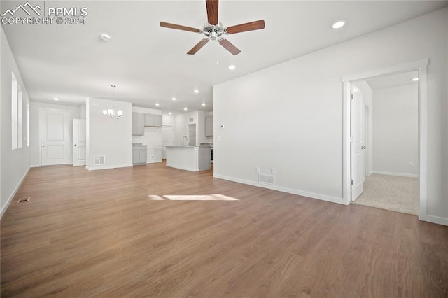 unfurnished living room featuring ceiling fan with notable chandelier and hardwood / wood-style flooring