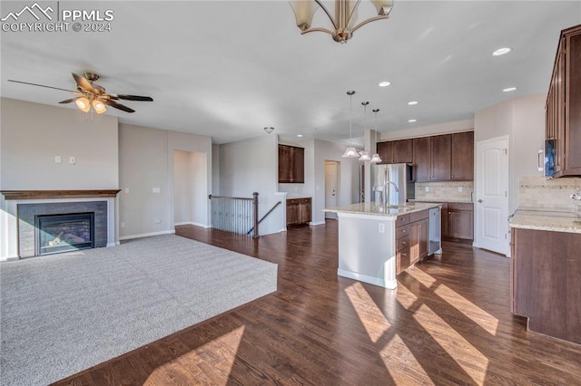 kitchen featuring dark wood-type flooring, pendant lighting, decorative backsplash, and a center island with sink